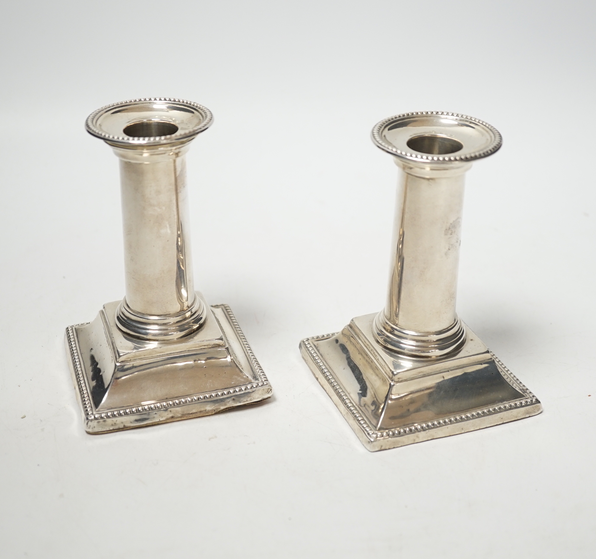 A pair of late Victorian silver dwarf candlesticks, with beaded borders, Edward Hutton, London, 1882, 11.7cm, weighted.